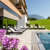 Modern hotel poolside with lounge chairs, surrounded by lush green landscape and mountains, at Wellnesshotel Klosterhof in Bayern.