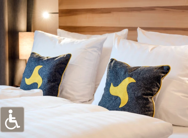 Gemütliches Doppelbett mit Kissen in grau und gelb, sanft beleuchtet, ideal für einen entspannten Aufenthalt im Klosterhof.
