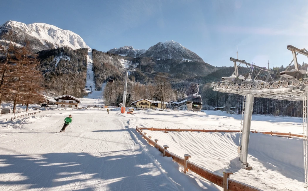 Skiers on a sunny slope with snowy mountains in the background, near Wellnesshotel Klosterhof in Bayern.