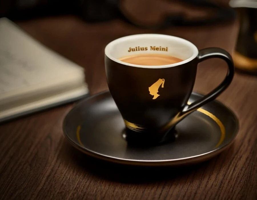 Eine elegante Tasse Kaffee auf einem Unterteller, mit dem Logo von Julius Meinl, auf einem Holztisch.