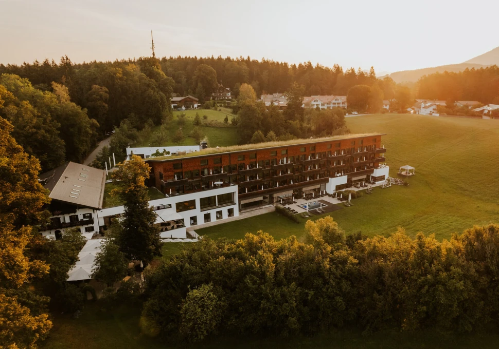 Ein modernes Hotelgebäude inmitten von Bäumen und Wiesen, bei Sonnenuntergang, umgeben von einer idyllischen Landschaft.