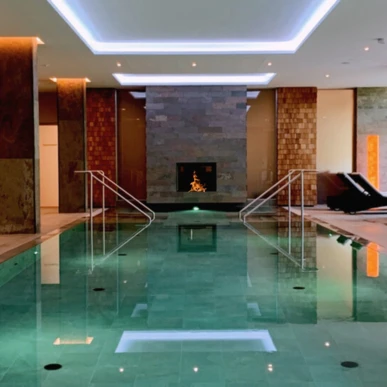 Luxurious indoor pool at Wellnesshotel Klosterhof in Bayern, featuring lounge chairs and a cozy fireplace ambiance.