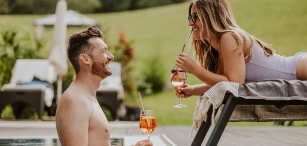 Ein Mann und eine Frau genießen Cocktails am Pool im Hotel Klosterhof, umgeben von einer grünen Landschaft in Bayern.