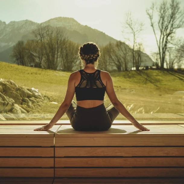 Eine Person meditiert in einem Wellnessbereich des Hotel Klosterhof mit Blick auf die Alpen in Bayerisch Gmain.