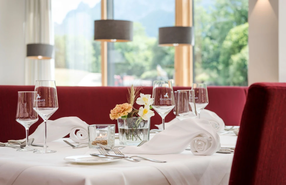 Elegant table setting with wine glasses, folded napkins, and a flower centerpiece in a bright restaurant at Klosterhof.