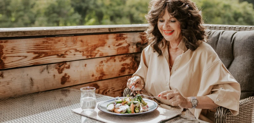 Eine Frau genießt eine gesunde Mahlzeit auf einer Terrasse mit Blick auf die Natur, umgeben von Holzverkleidung.