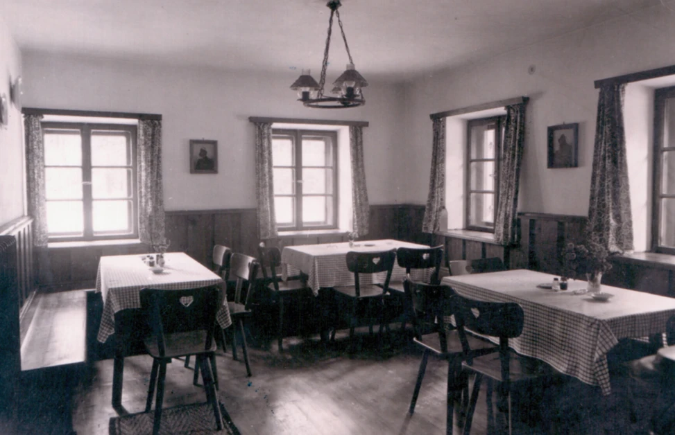 A vintage dining room with checkered tablecloths, wooden chairs, and windows with patterned curtains at Hotel Klosterhof.