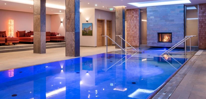 Indoor pool area with modern design, featuring blue lighting, a cozy fireplace, and comfortable seating.