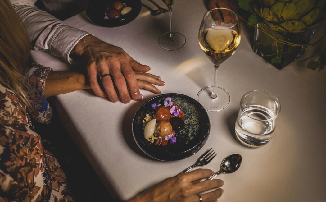 Ein Paar genie&szlig;t ein stilvolles Abendessen bei Kerzenschein, mit Dessert und Wei&szlig;wein auf einem elegant gedeckten Tisch.
