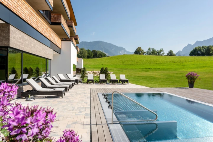 Ein moderner Außenbereich des Hotel Klosterhof mit Liegen und einem Pool, umgeben von grünen Wiesen und Bergen in Bayerisch Gmain.