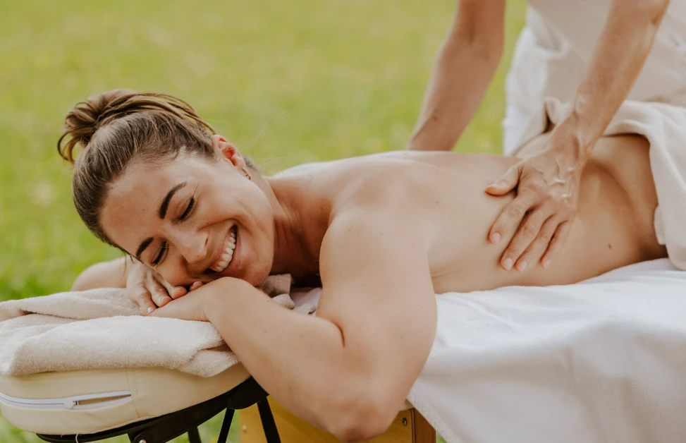 A woman enjoys a relaxing outdoor massage on a table, smiling with eyes closed.
