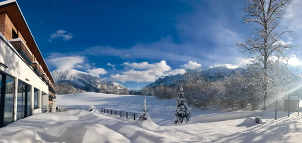 Schneebedeckte Landschaft mit Blick auf die Berge und das Hotel Klosterhof in Bayerisch Gmain. Helle, sonnige Atmosphäre.