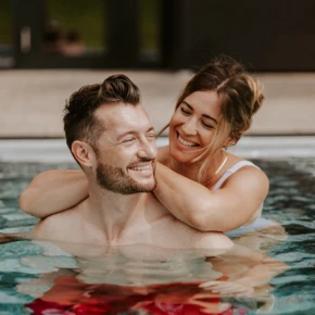 Ein Paar entspannt im Pool des Hotel Klosterhof, lächelnd und glücklich, umgeben von einer idyllischen Wellnessatmosphäre in Bayern.