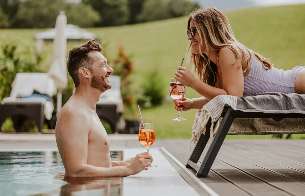 Ein Mann und eine Frau genießen Cocktails am Pool im Hotel Klosterhof, umgeben von einer grünen Landschaft in Bayern.