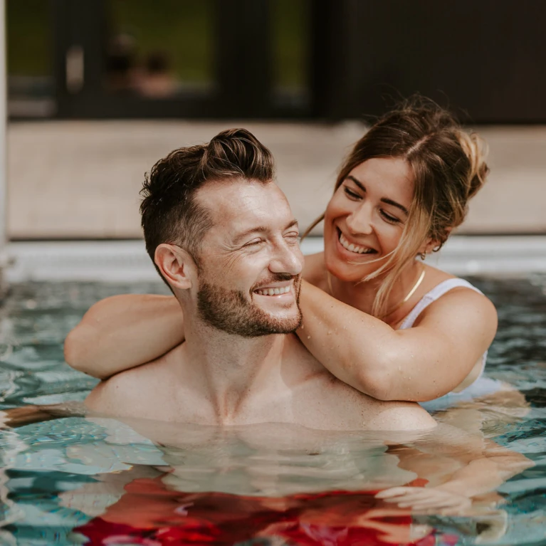 Ein Paar entspannt im Pool des Hotel Klosterhof, lächelnd und glücklich, umgeben von einer idyllischen Wellnessatmosphäre in Bayern.