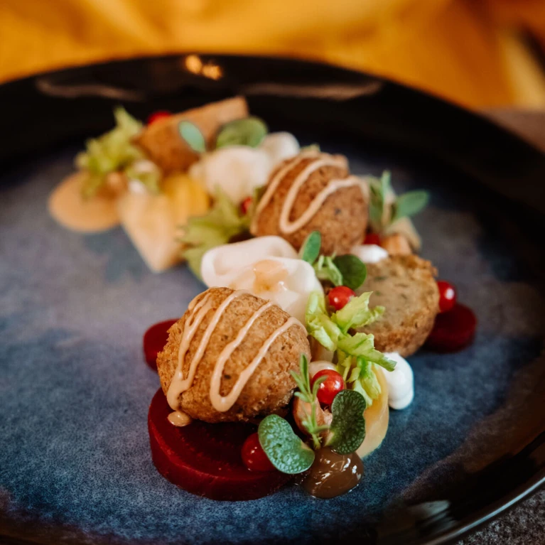 Ein kunstvoll angerichteter Teller mit knusprigen Bällchen, frischen Kräutern und buntem Gemüse, serviert im Hotel Klosterhof.