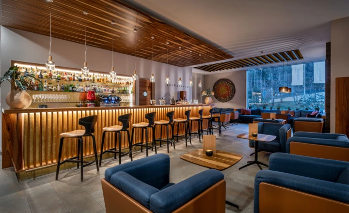 Moderne Bar mit beleuchtetem Tresen, stilvollen Stühlen und gemütlichem Sitzbereich. Fenster mit Blick ins Freie.