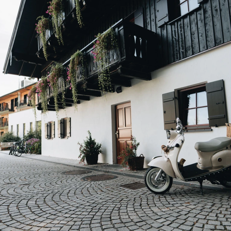 Ein charmantes Bild eines weißen Rollers vor einem traditionellen Gebäude mit Blumen und Fensterläden in Bayerisch Gmain.