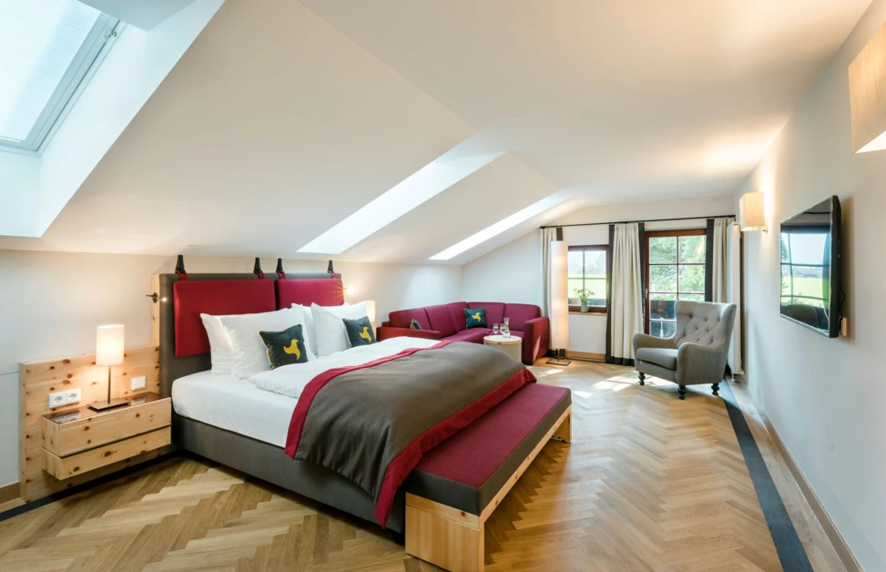 Spacious hotel room with elegant decor, featuring a large bed, cozy seating area, and natural light from skylights and windows.