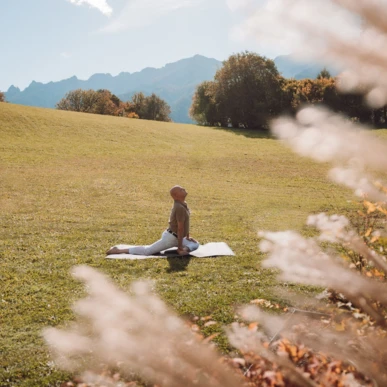 A person practices yoga in a serene meadow at Wellnesshotel Klosterhof, surrounded by autumn trees and distant mountains.