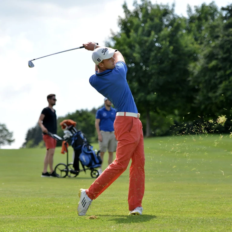 Ein Golfer schwingt seinen Schläger auf einer gepflegten Golfbahn, während Zuschauer im Hintergrund entspannen.