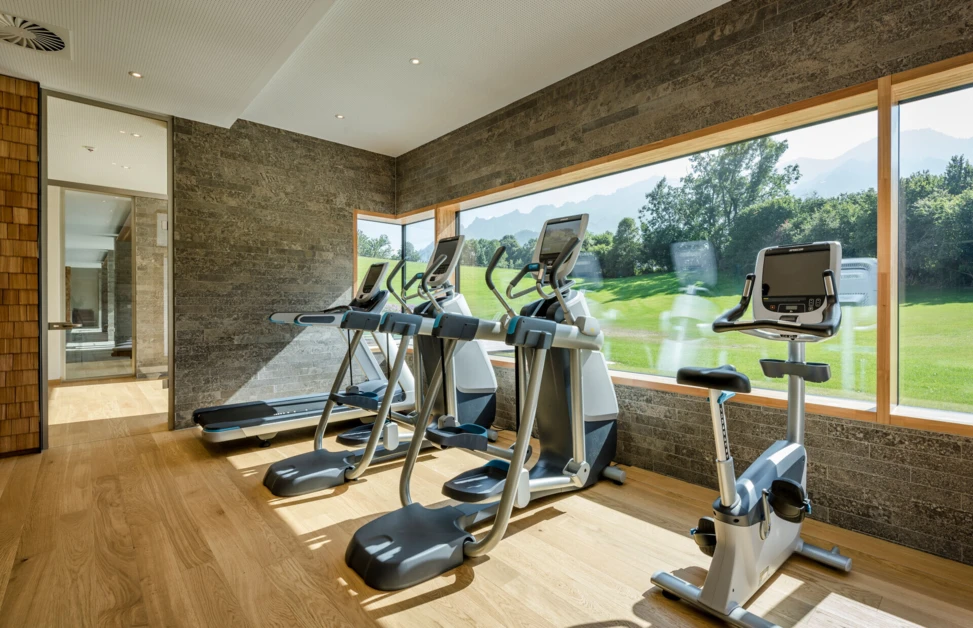 Fitness room with treadmills and exercise bikes, overlooking a scenic view through large windows.