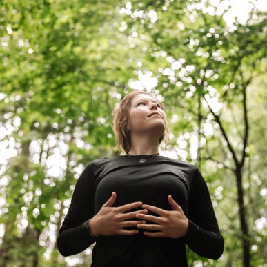 Eine Person steht in einem Wald, schaut nach oben und genießt die Natur um sich herum.