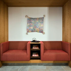 Ein gemütlicher Sitzbereich mit roten Sofas und buntem Wandkunstwerk, umgeben von Holzverkleidung.