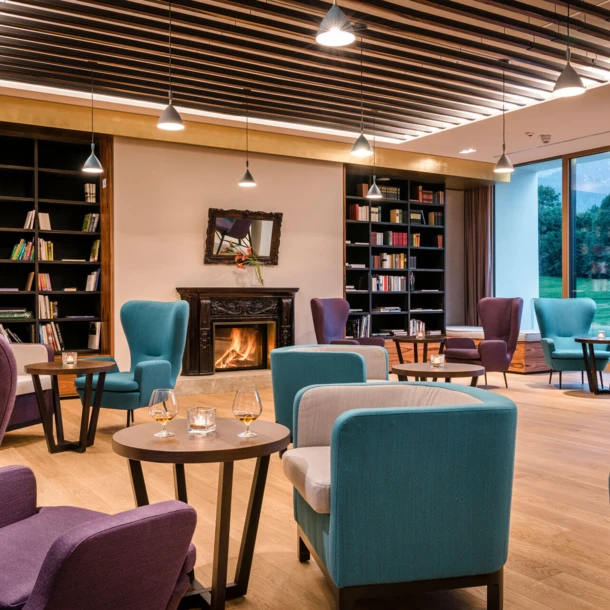 Gemütlicher Lounge-Bereich im Hotel Klosterhof mit Leserecke, bequemen Sitzgelegenheiten und Kamin, umgeben von natürlichem Licht.