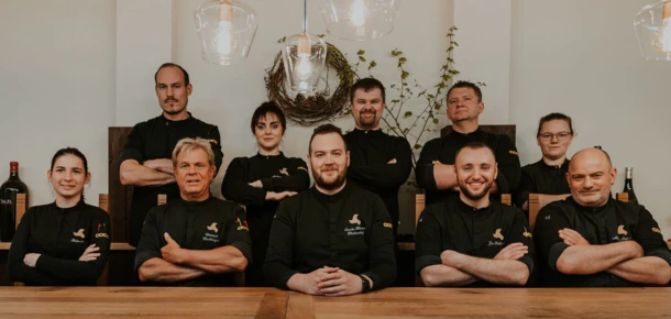 Ein Team von Köchen posiert lächelnd vor einem Holztisch in einem modernen Restaurant.