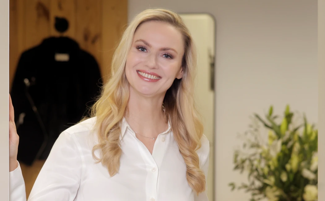 Eine lächelnde Frau in einem weißen Hemd steht an einer Tür und begrüßt Gäste im Hotel Klosterhof, einem Wellnesshotel in Bayern.