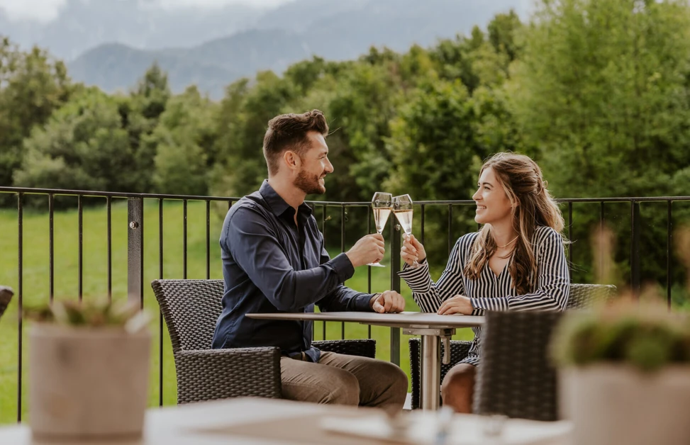 Ein Paar steht auf dem Balkon ihres Hotelzimmers und genießt den Ausblick auf die Bergwelt im Berchtesgadener Land.