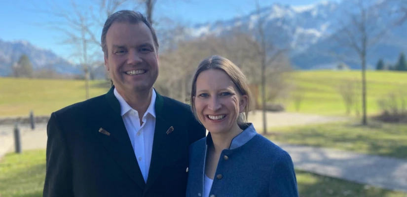 A smiling man and woman stand outdoors with mountains in the background, capturing a serene moment at Hotel Klosterhof.