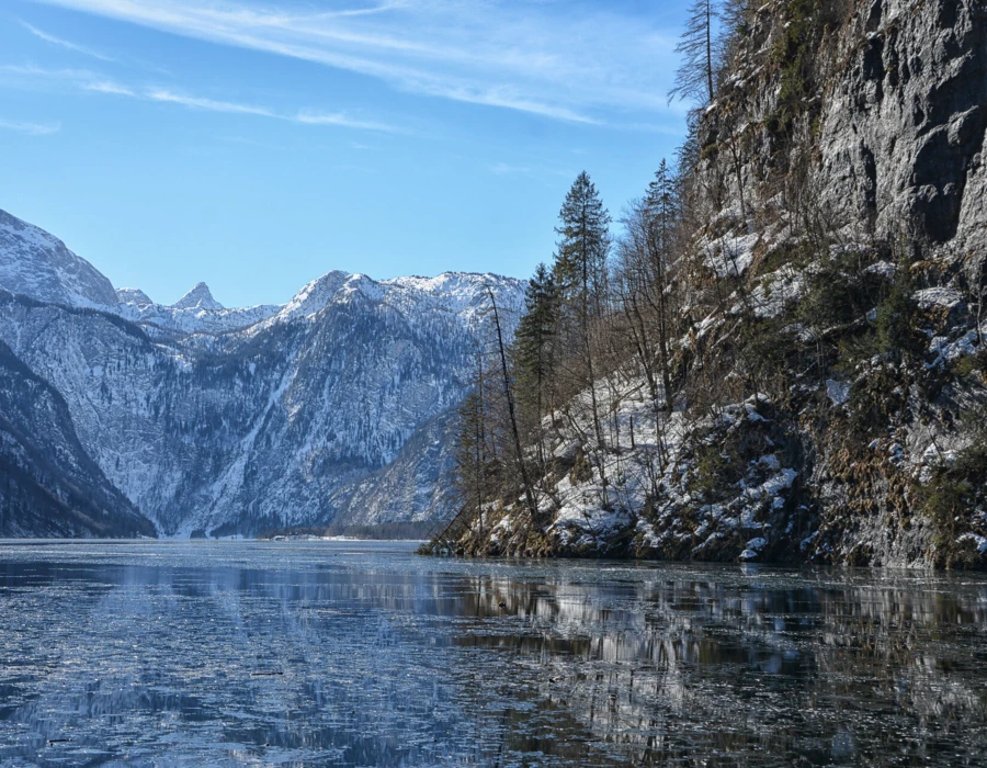 Ein klarer Wintertag am See, umgeben von schneebedeckten Bergen und spiegelndem Wasser. Ideal für Naturliebhaber und Erholungssuchende.