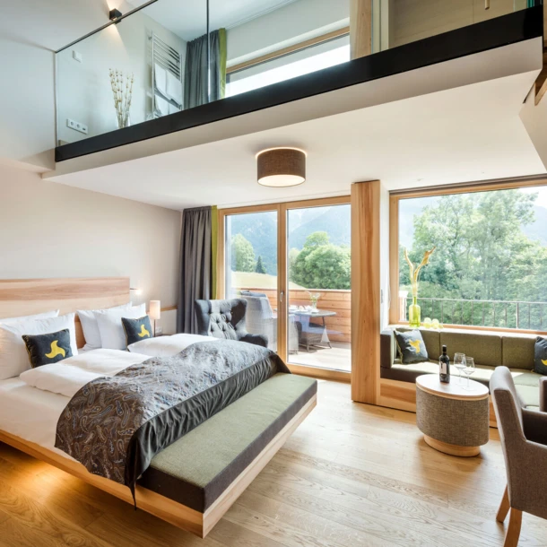 Modern hotel room with a loft, featuring a large bed, seating area, and balcony with mountain views at Hotel Klosterhof.