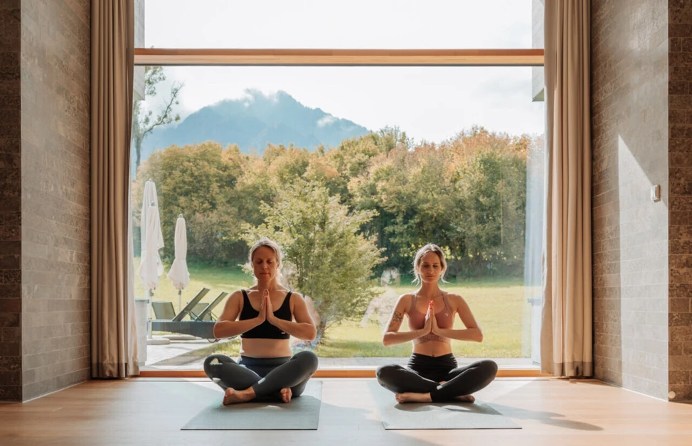 Zwei Frauen meditieren auf Yogamatten im Hotel Klosterhof, umgeben von der Natur und den Alpen in Bayerisch Gmain.
