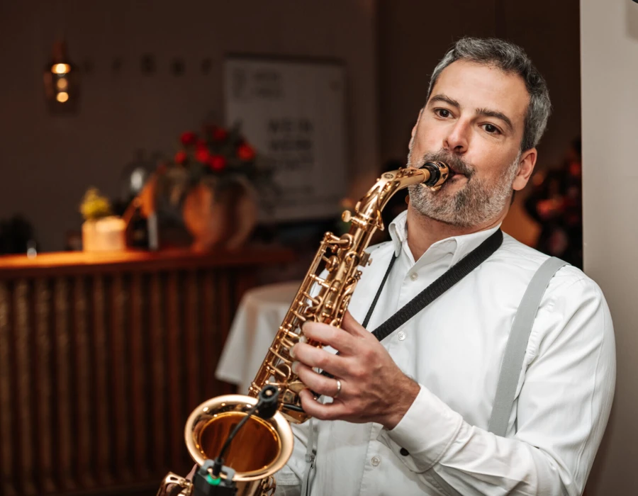 A man in a white shirt plays the saxophone in a cozy, ambient setting at Hotel Klosterhof.
