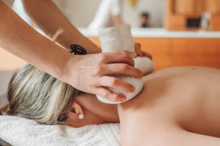 Eine Person erh&auml;lt eine wohltuende Massage mit hei&szlig;en Kr&auml;uterstempeln in einem Wellnessbereich. Entspannung und Erholung im Hotel Klosterhof.