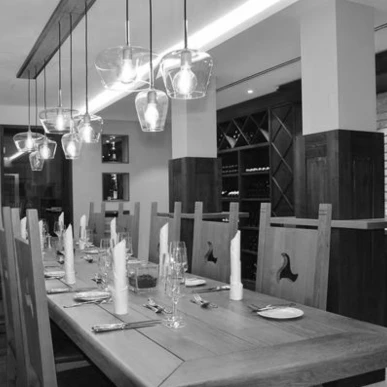 Ein eleganter Speisesaal mit rustikalem Holztisch, modernen Lampen und stilvollem Geschirr, ideal f&uuml;r gesellige Anl&auml;sse.