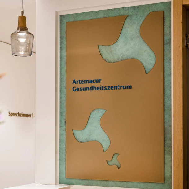 Ein Empfangsbereich mit einem stilvollen Schild des Artemacur Gesundheitszentrums und einer blühenden Blumenarrangement im Vordergrund.