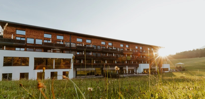Moderne Fassade des Hotel Klosterhof in Bayerisch Gmain, umgeben von Wiese und Alpen bei Sonnenuntergang. Wellnesshotel mit alpinem Charme.