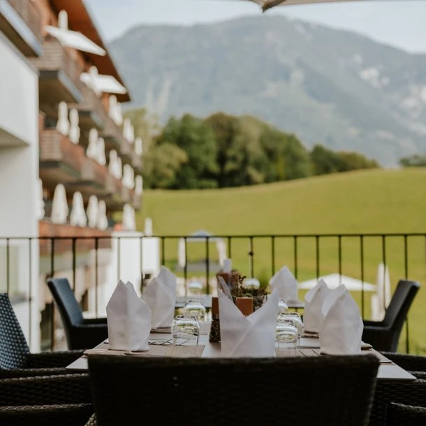 Outdoor dining area with set table, wicker chairs, and mountain view at a hotel.