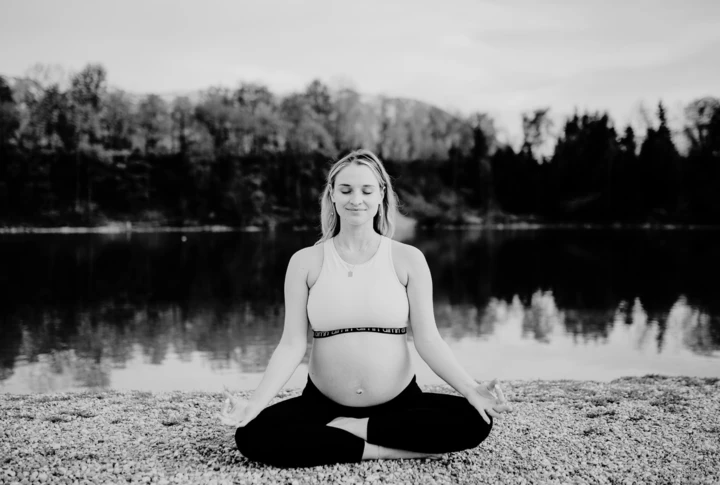Schwangere Frau meditiert am Ufer eines Sees, umgeben von Natur, bei Ruhe und Entspannung im Wellnesshotel Klosterhof, Bayern.
