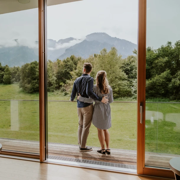 Ein Paar genießt die Aussicht auf die Alpen von ihrem Zimmer im Hotel Klosterhof, umgeben von Natur und Ruhe.