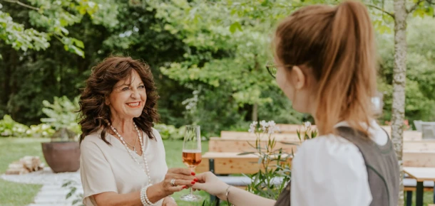 A woman in a garden receives a glass of rosé from a server.