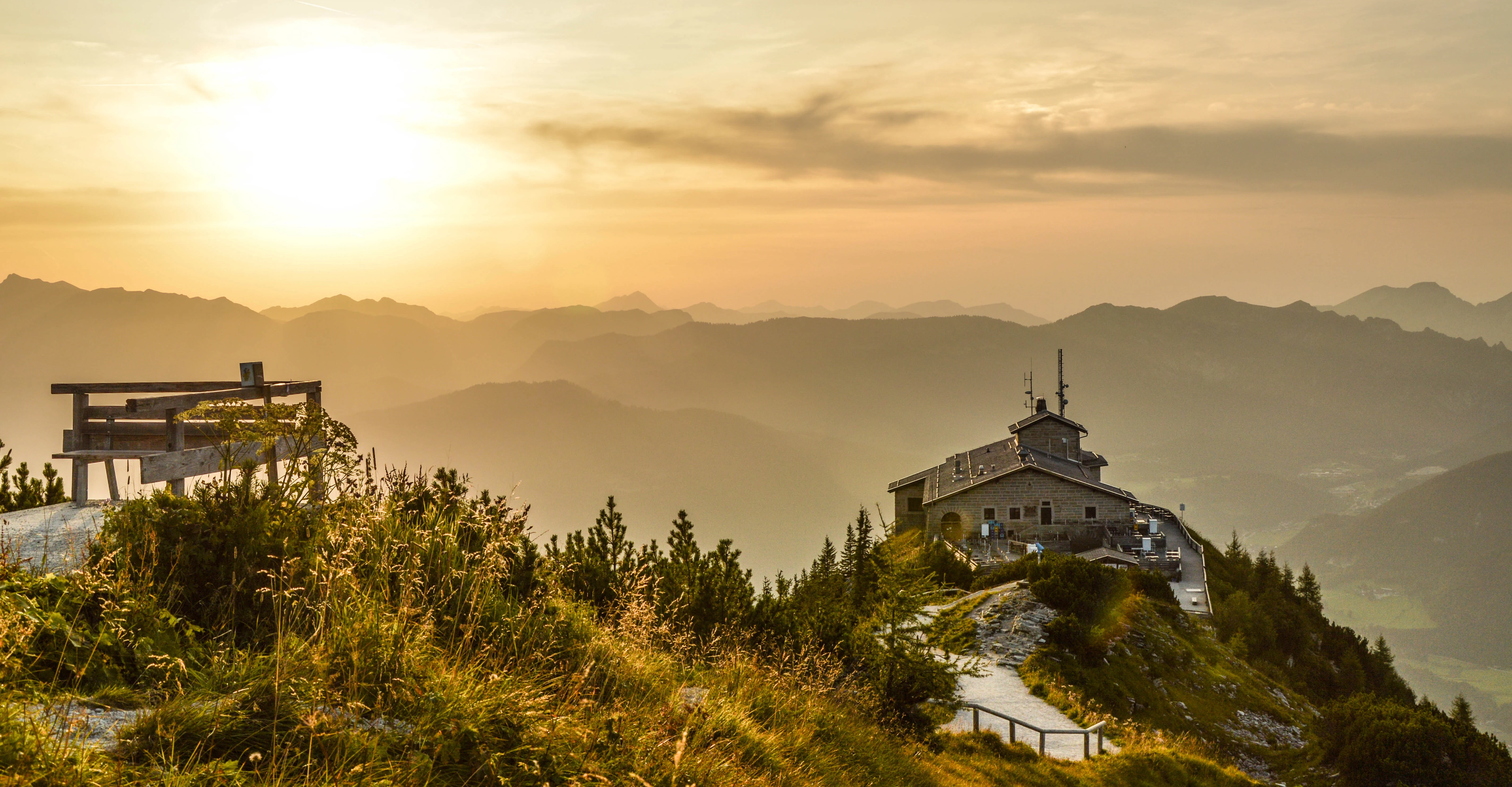 Mountain lodge at sunrise with panoramic views and a wooden bench in the foreground.