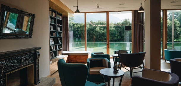 Elegant lounge with modern chairs, a fireplace, and large windows overlooking lush greenery, creating a serene and inviting atmosphere.