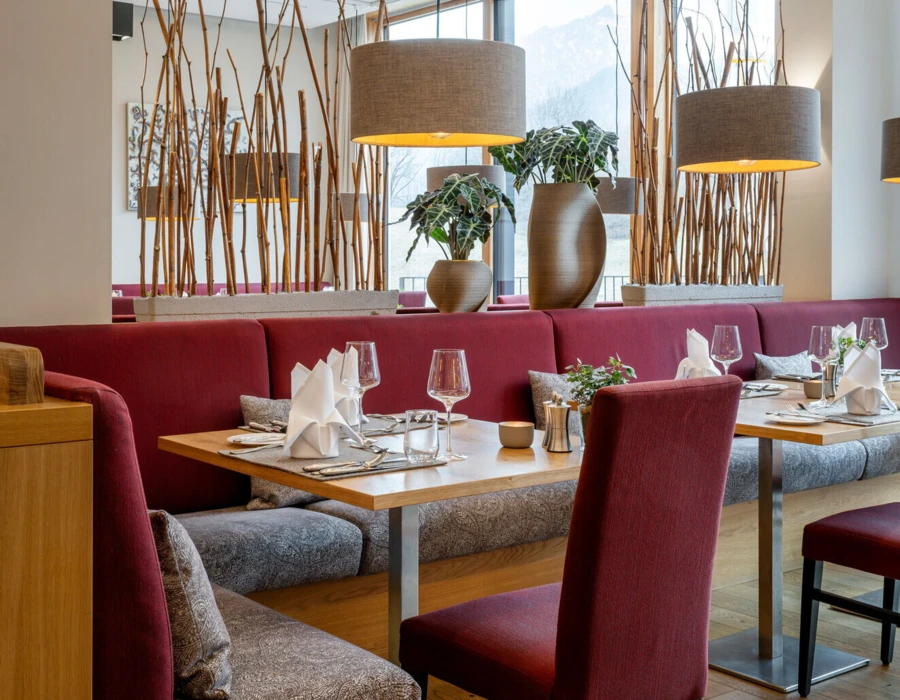 Elegant restaurant interior with red seating, wooden tables, and modern decor, including large vases and pendant lights, creating a cozy atmosphere.