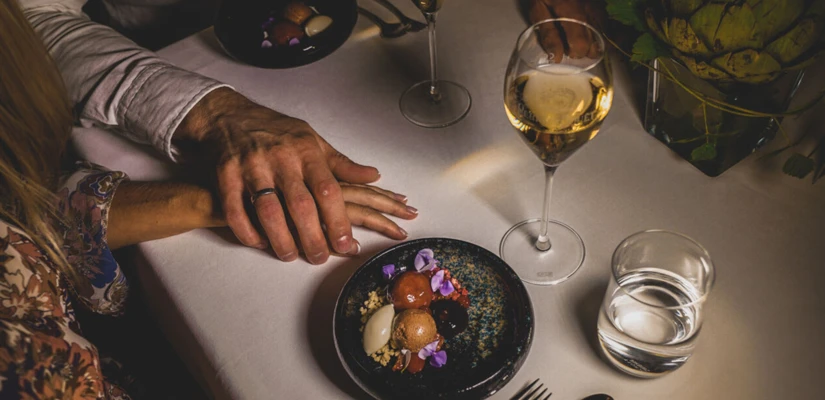 Couple holding hands over a table with dessert, wine, and a glass of water, creating a romantic dining atmosphere.