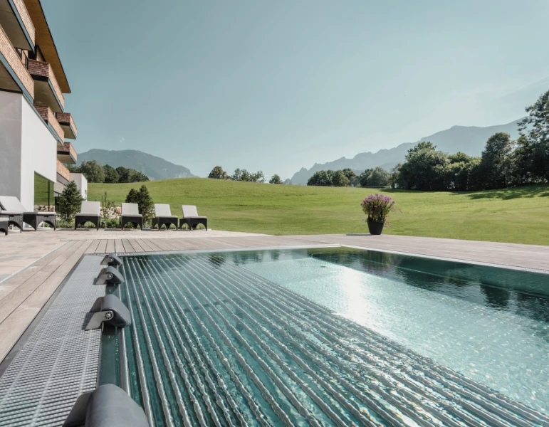 Ein moderner Pool mit Liegen, umgeben von einer großzügigen Wiese und Bergen im Hintergrund, ideal für Entspannung und Erholung.